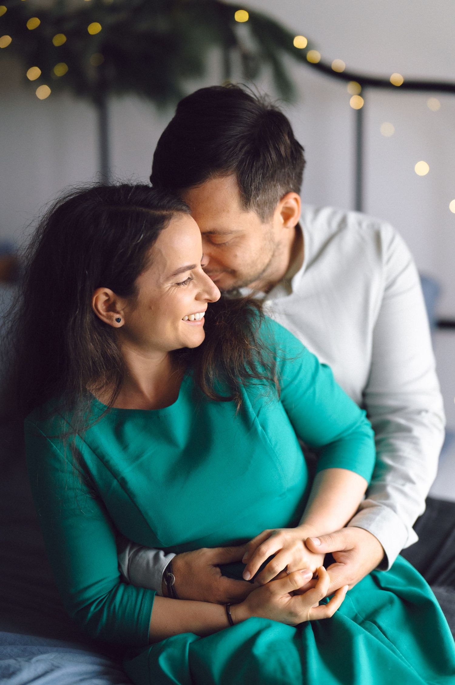 Candid photo series of couple sharing intimate laughing moments together on couch with soft bokeh lights in background.