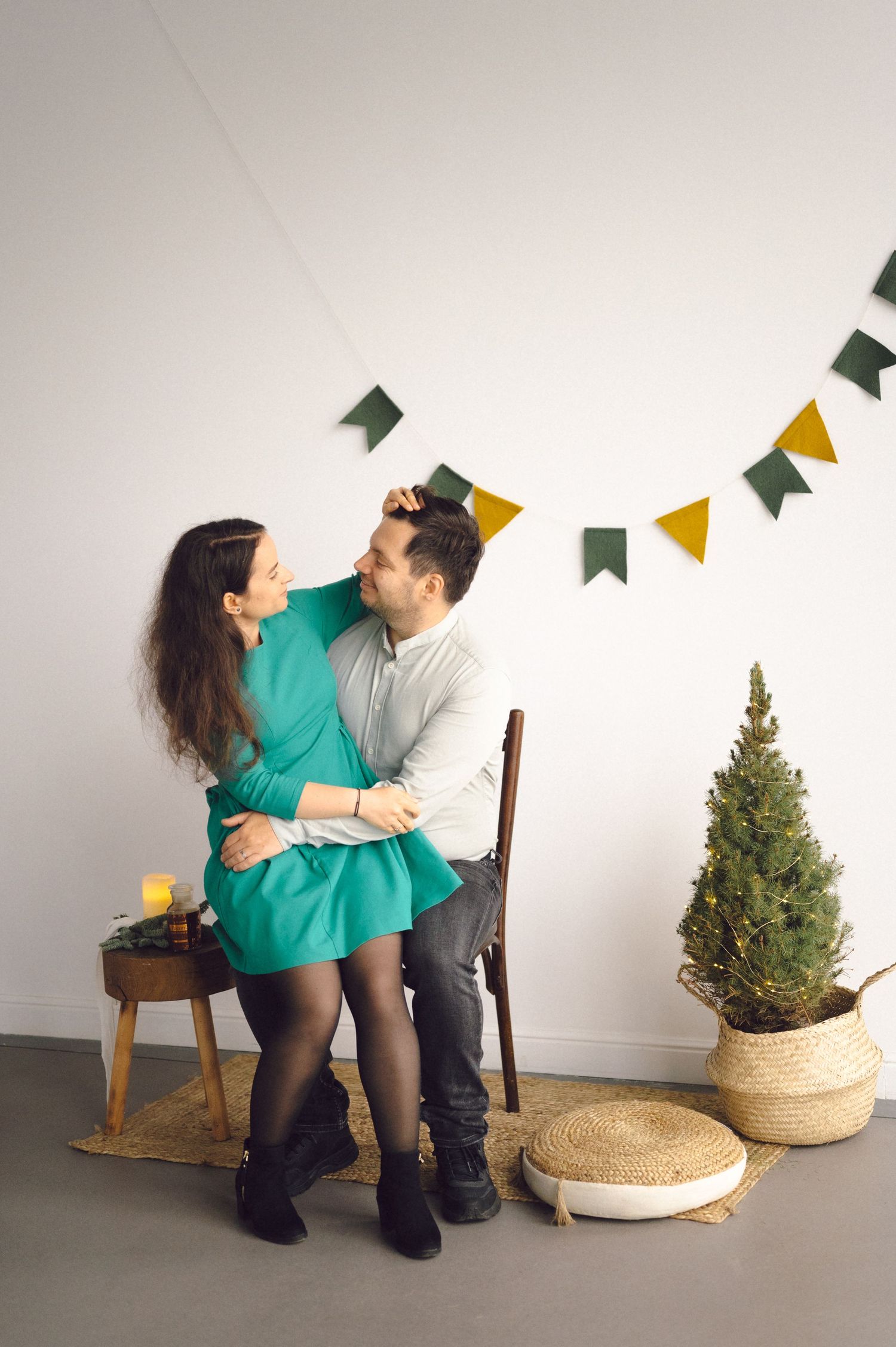 A couple in matching turquoise and white outfits dancing together near a small Christmas tree in a simple white room.