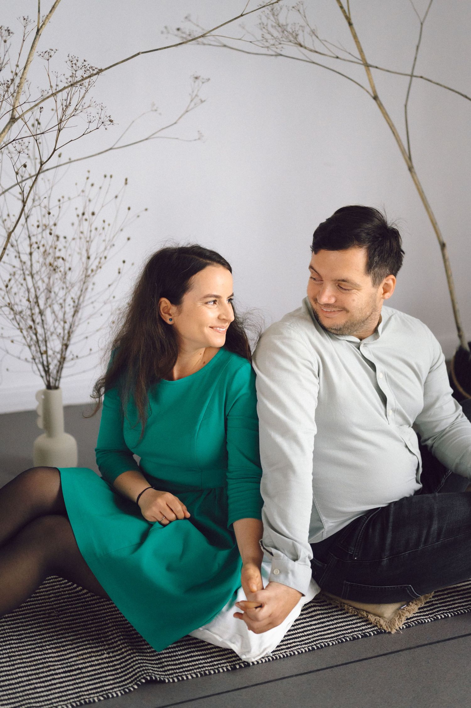 Couple in green and white outfits share intimate moments on a striped blanket during indoor photoshoot.