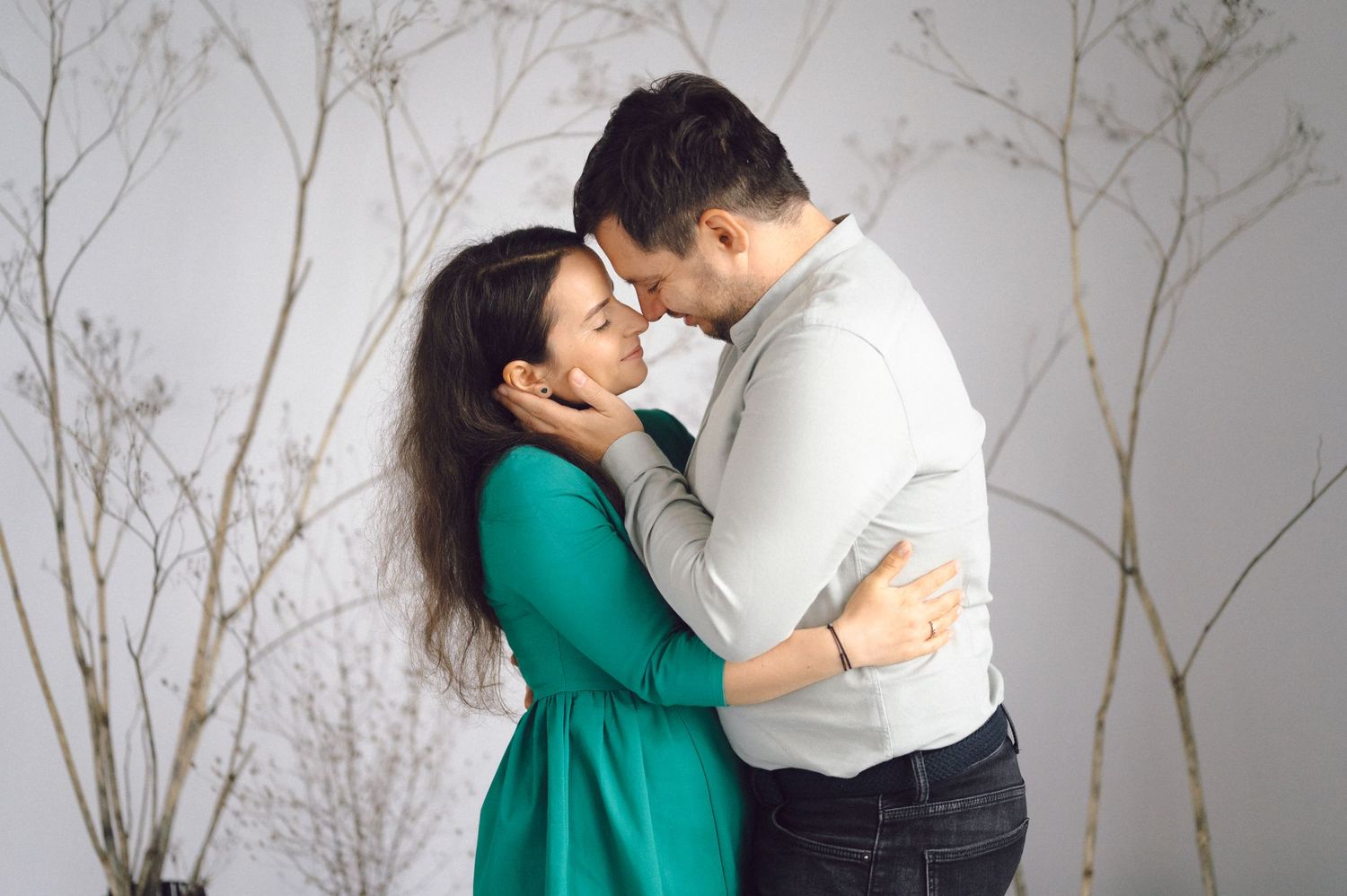 A romantic couple share an intimate moment against a gray background with bare branches.