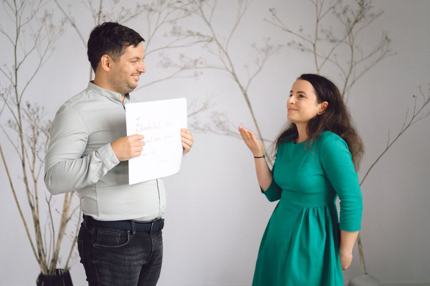 Two people in green and white outfits interact playfully in a minimalist room setting.