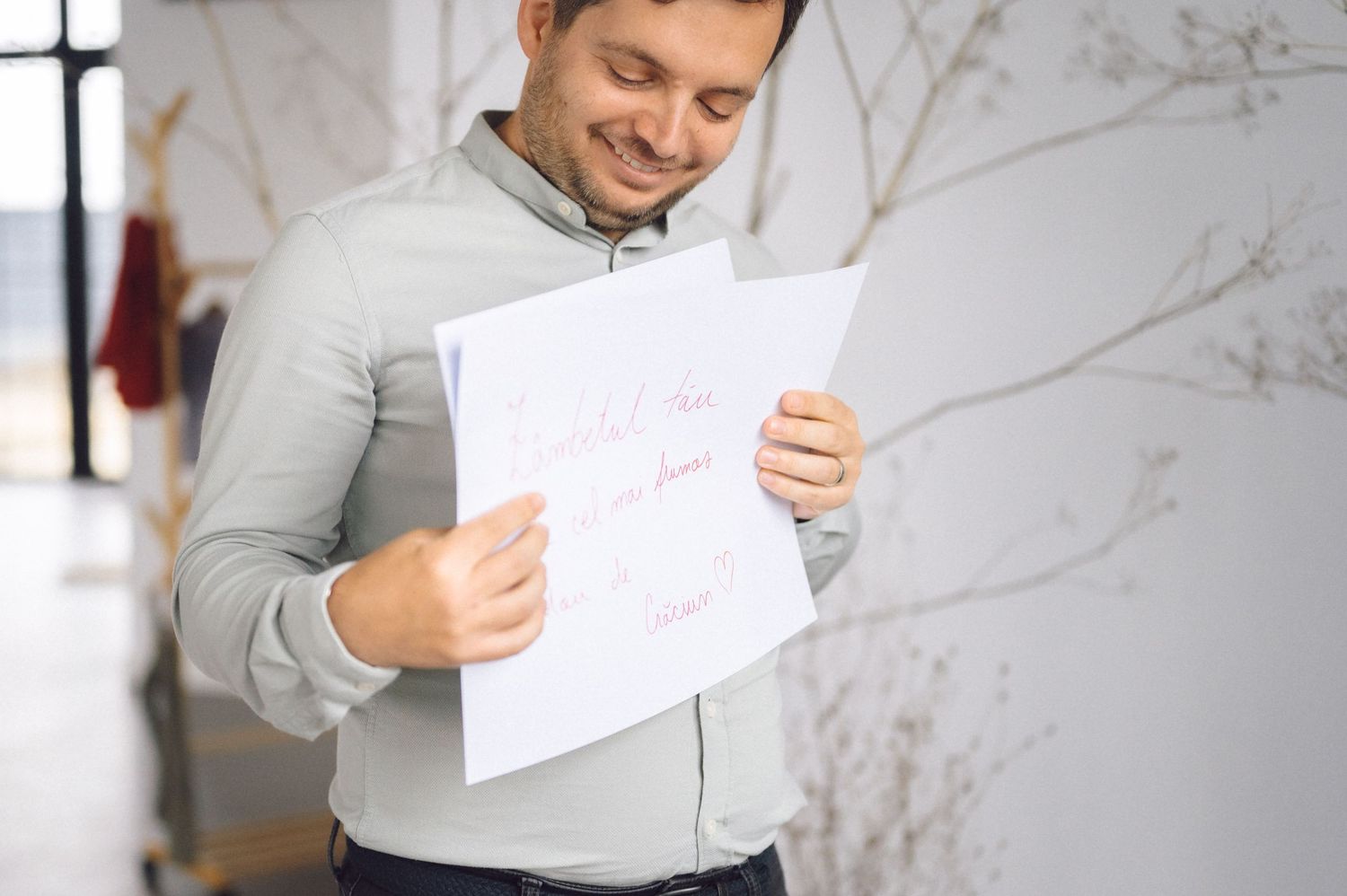 Someone wearing a gray sweatshirt smiles while reading a document in an indoor setting.