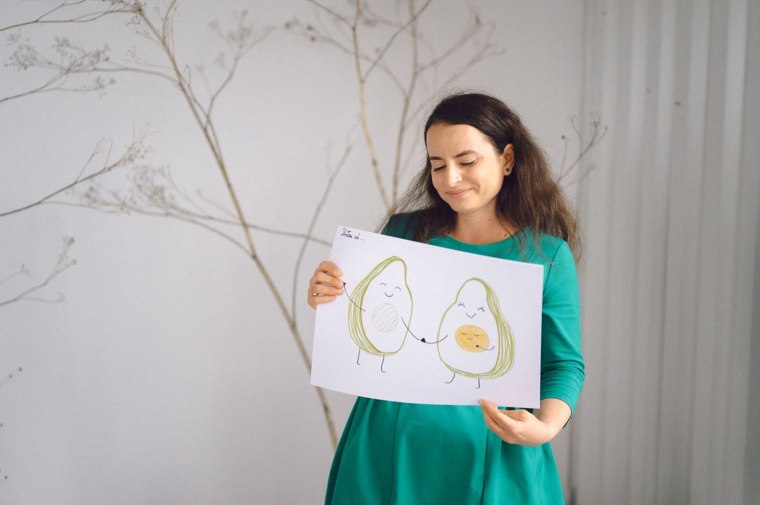 Person in green dress holds up a drawing of simple animal artwork against a white background.