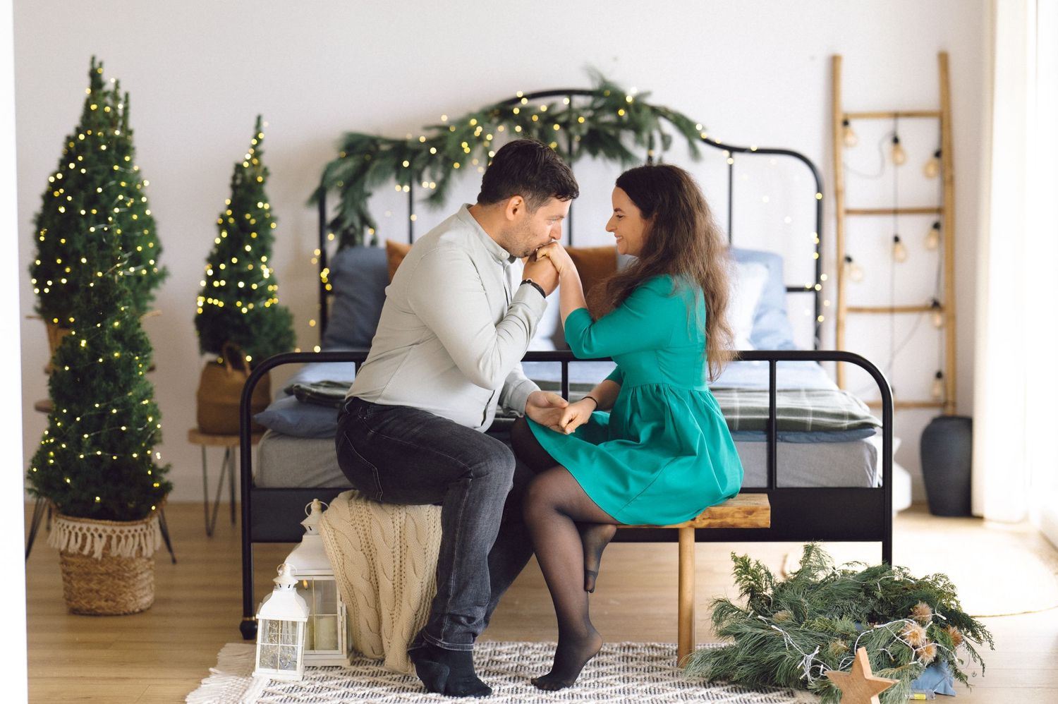 Romantic holiday scene with christmas trees and decor as couple embraces in white interior space.