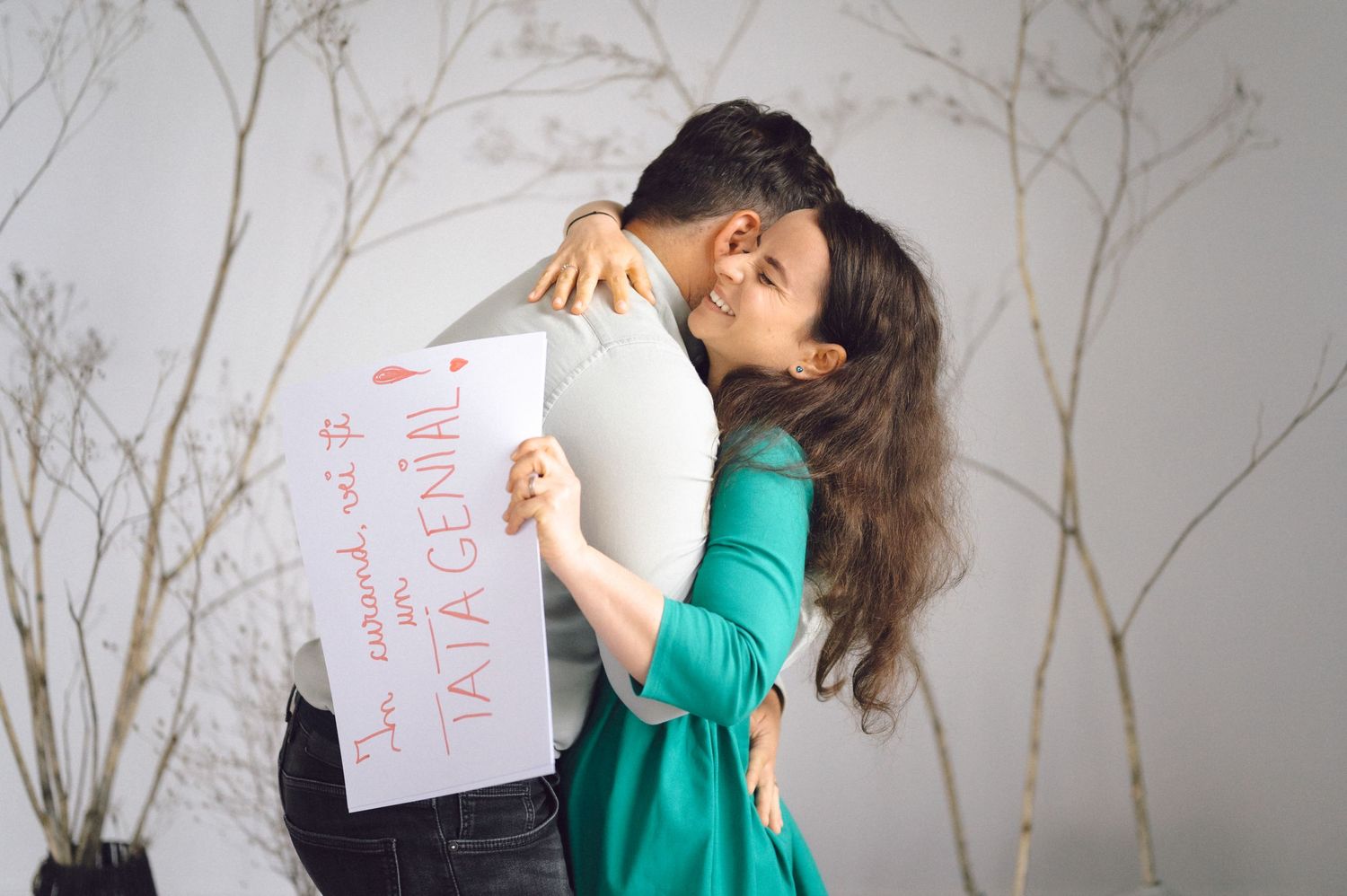 A person in green dress hugging someone holding a white paper sign with text in studio setting.