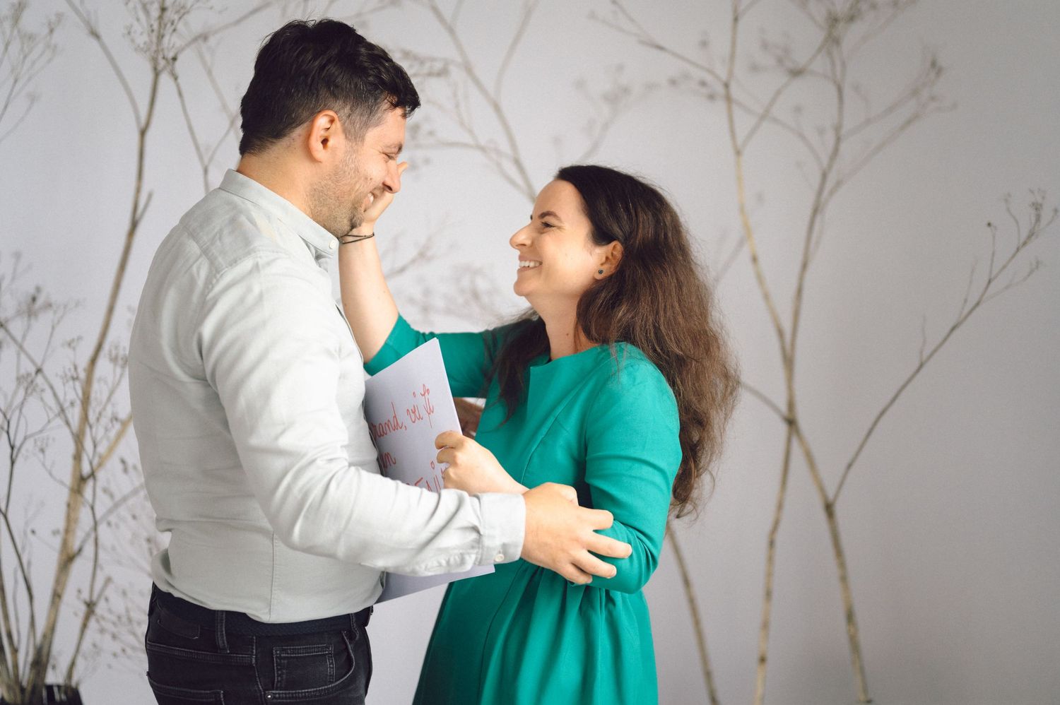 A couple in white and teal outfits shares romantic moments in a professionally styled photoshoot against a light backdrop.