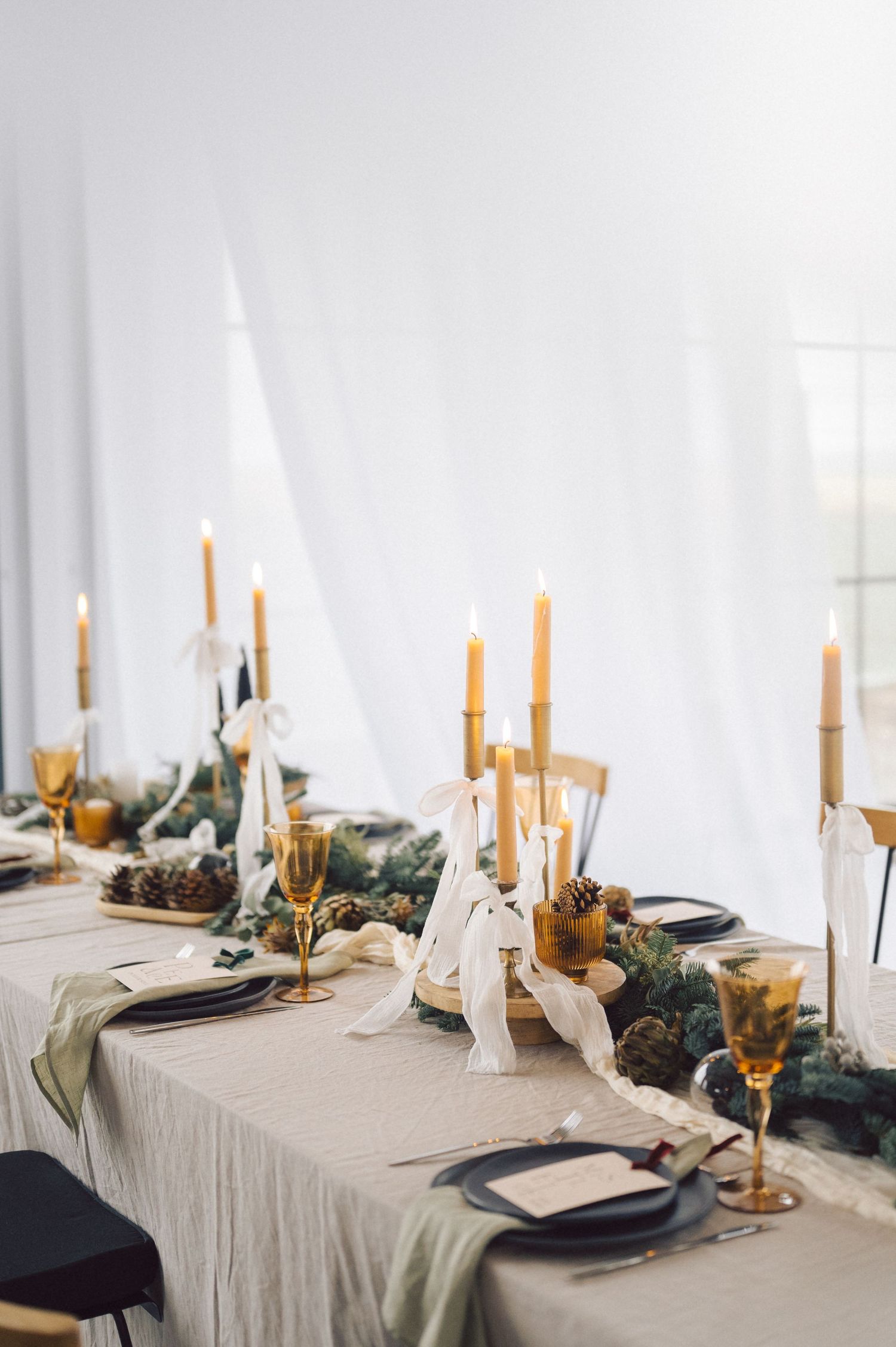 Elegant table setting with amber candlesticks, linen tablecloth, and greenery garland for a modern minimalist wedding reception.