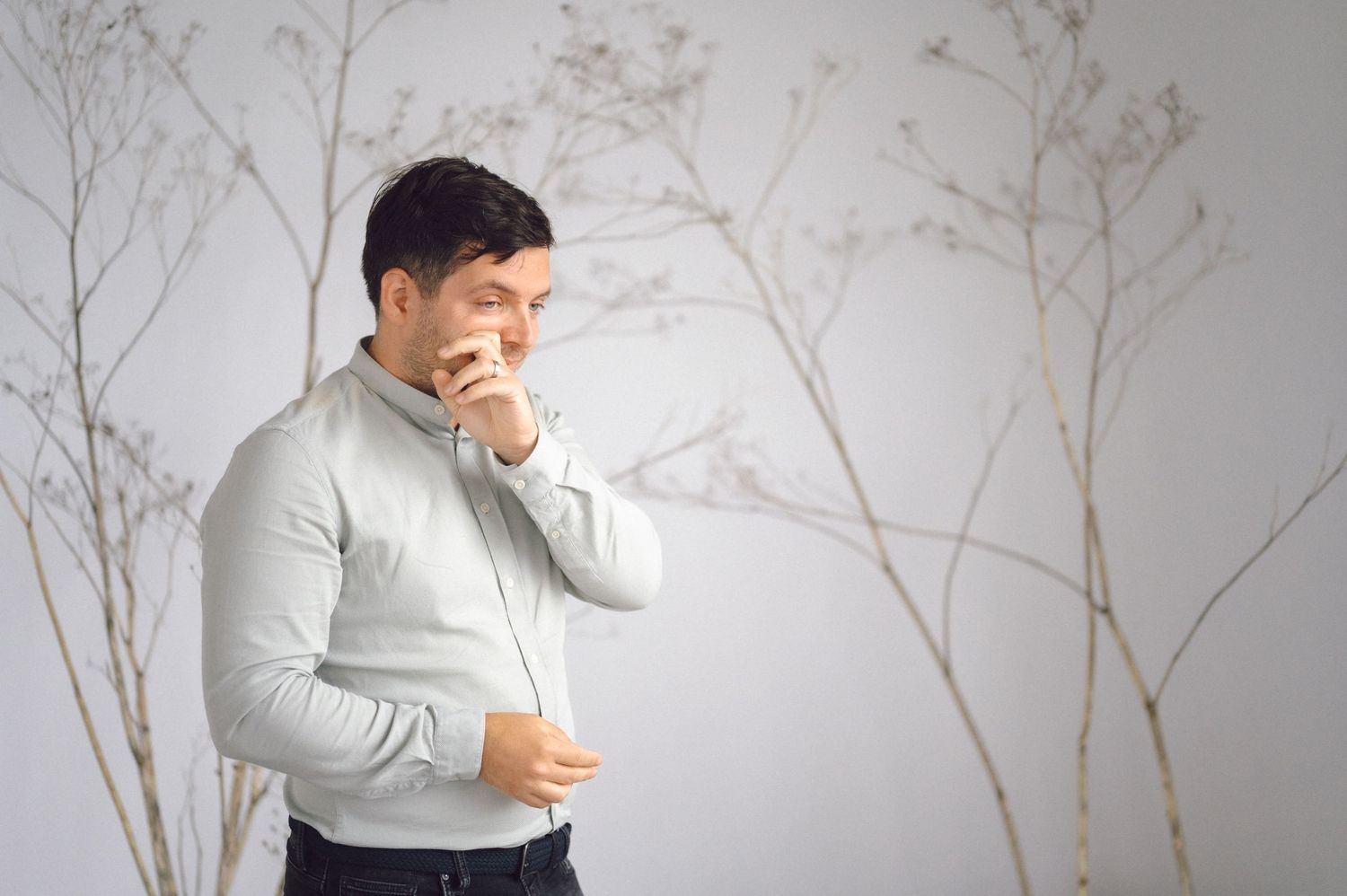 Man in white sweater laughing while looking at mobile device in front of marble wall backdrop.