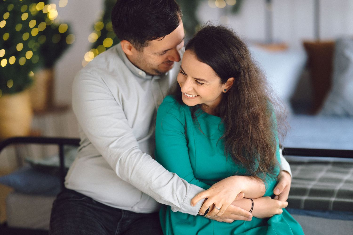 Tender moment captured in front of holiday decorations with bokeh lights creating festive atmosphere.