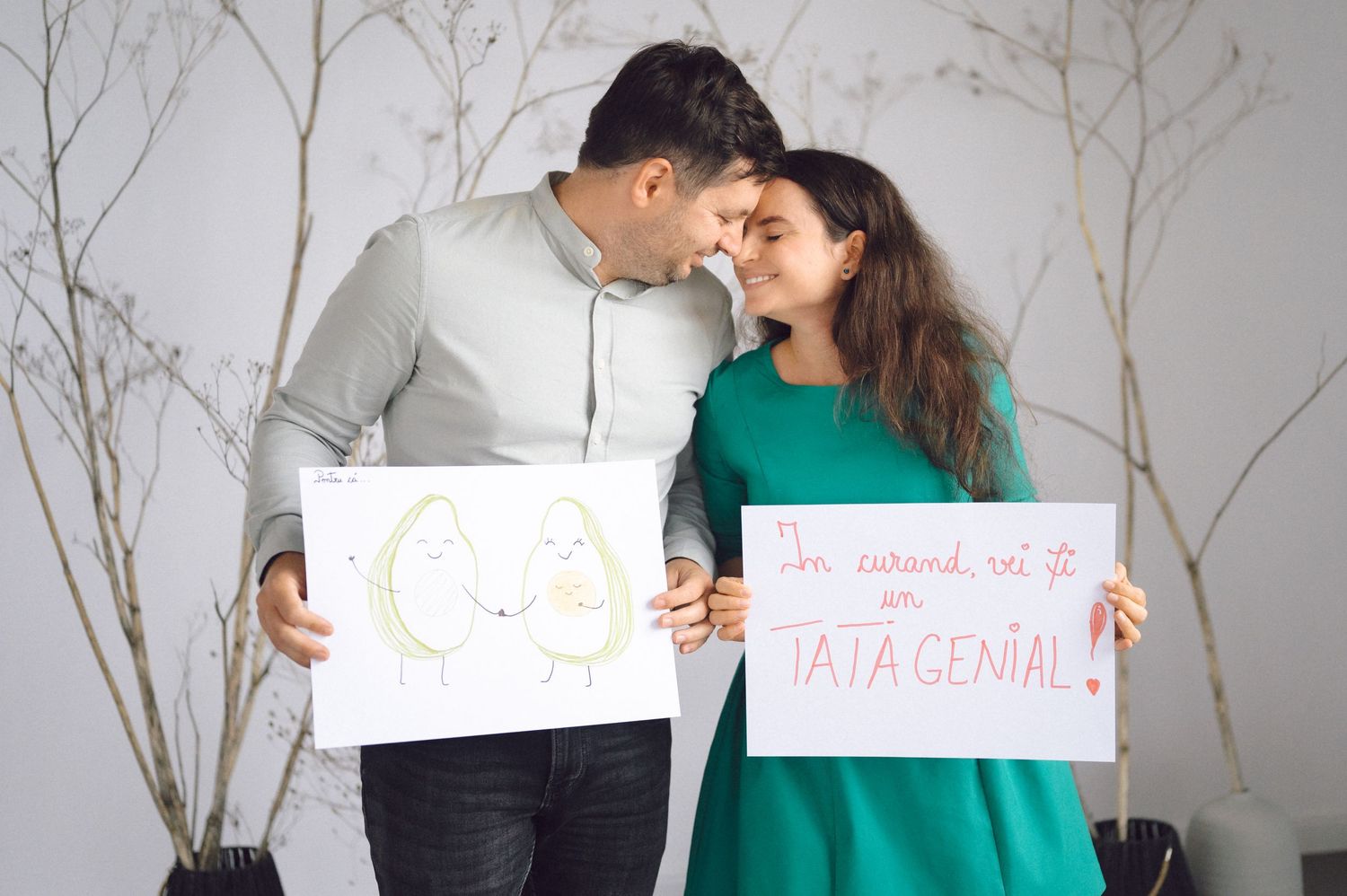 A couple hold up signs while sharing romantic moments in a photo collage against a white background with branches.