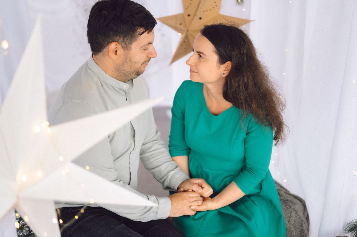 A couple in matching green and gray outfits share tender moments while sitting together on a white couch.