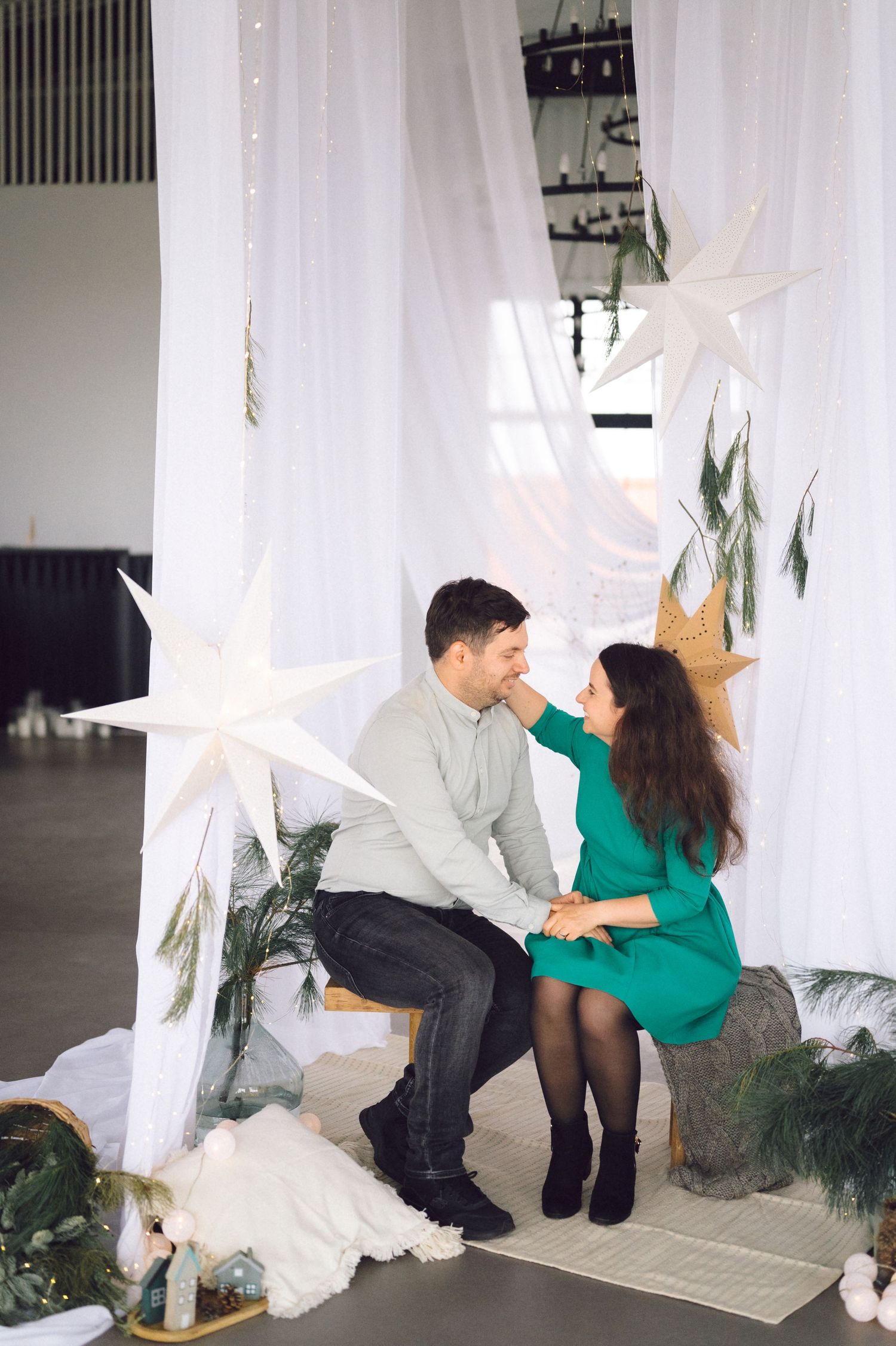 A couple shares an intimate moment on rustic seating surrounded by white curtains and decorative paper stars.