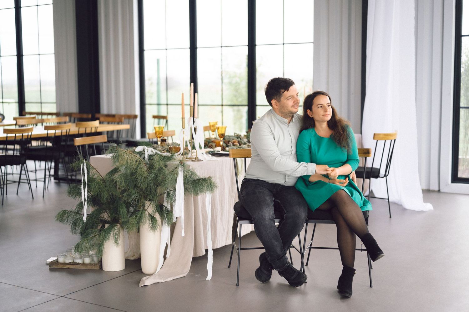 A couple poses together in a bright studio space with white walls and tall windows.