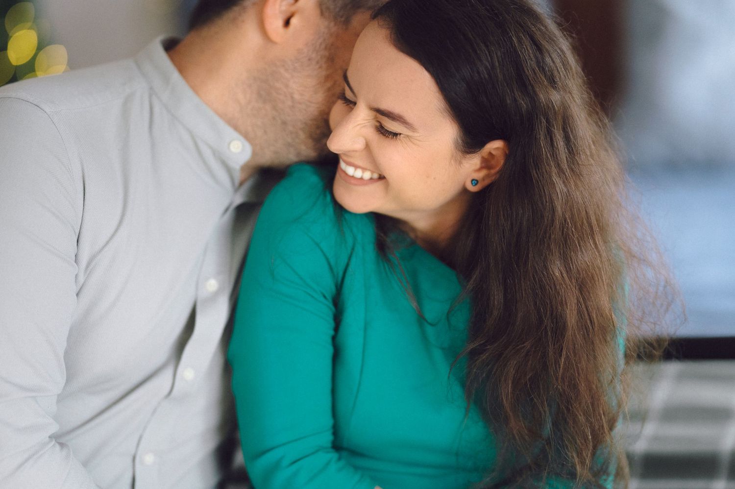 A romantic couple sharing an intimate moment, with one wearing a green sweater and the other in grey.