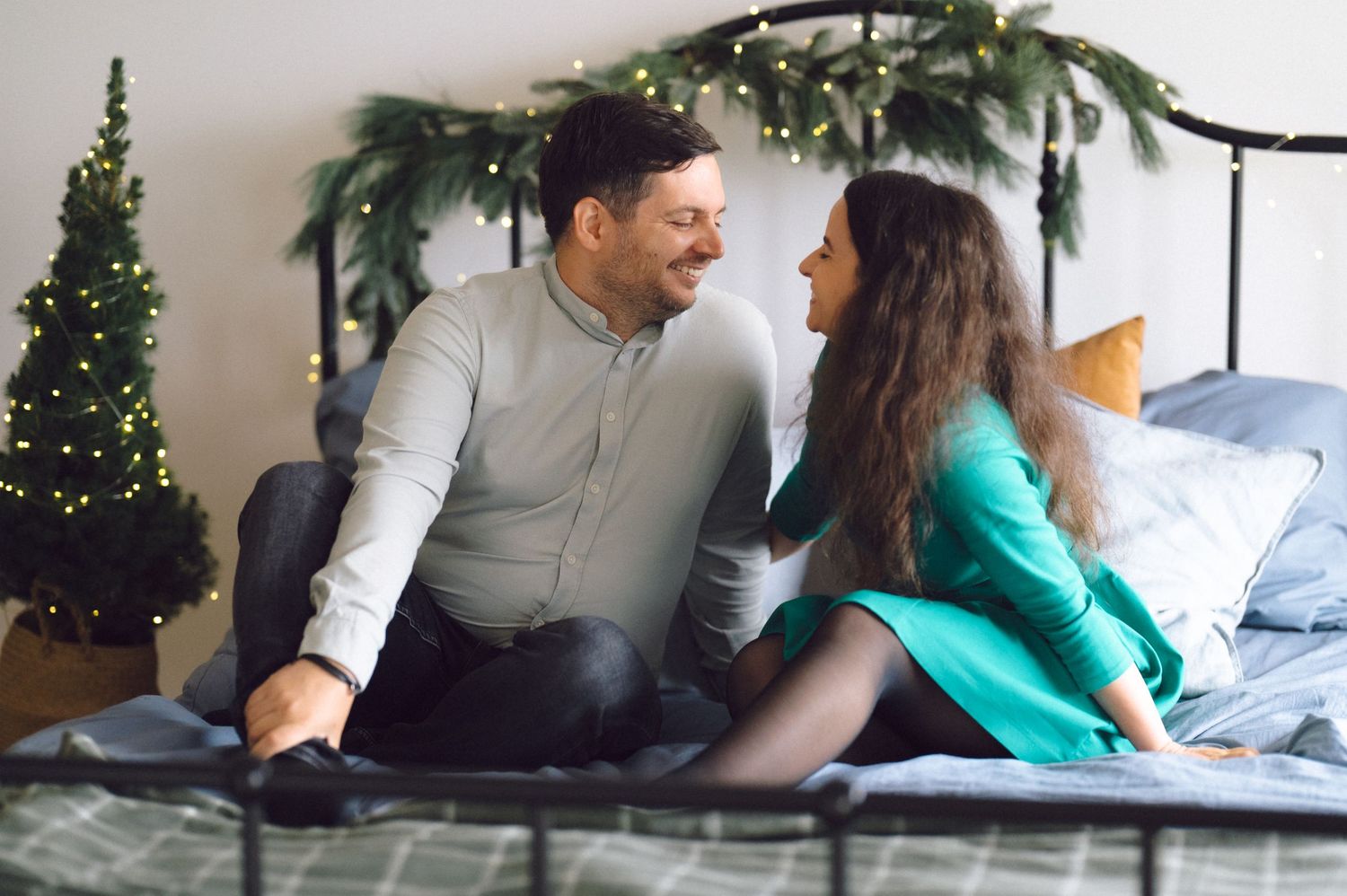 A couple shares a romantic moment on their bed with Christmas decorations and greenery in the background.