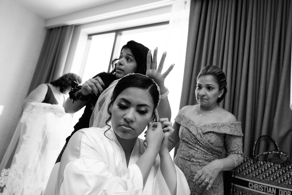 Black and white photo of wedding preparation moments in a hotel room with curtains.