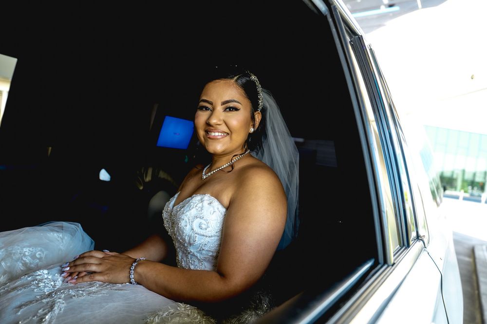 A bride wearing a strapless white wedding dress poses inside a luxury vehicle.