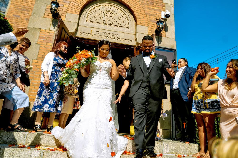 Newlyweds exit a brick church as guests celebrate on the steps under bright blue skies.
