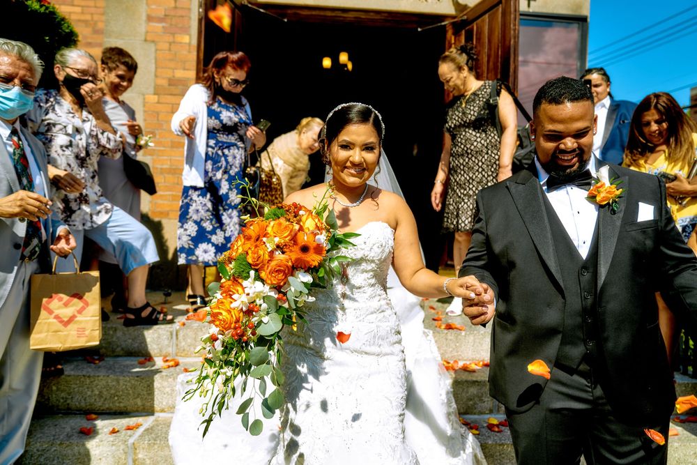 A couple exits their wedding ceremony while guests shower them with celebratory petals on church steps.