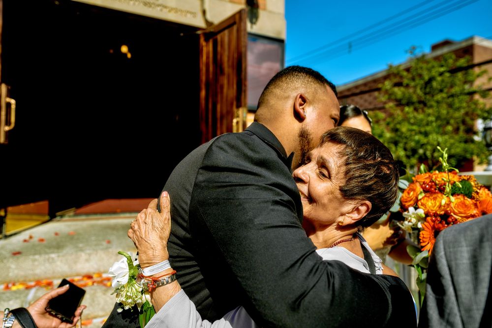 A tender embrace shared outside a historic brick church during a wedding celebration.