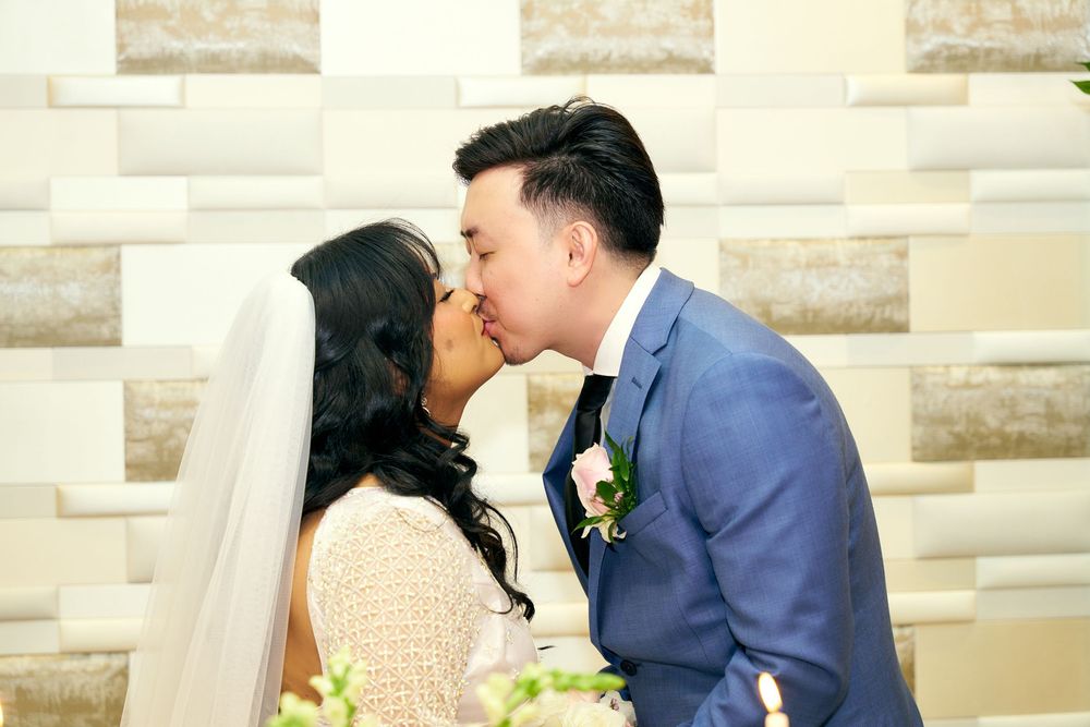 A romantic wedding kiss moment against a stone wall backdrop.
