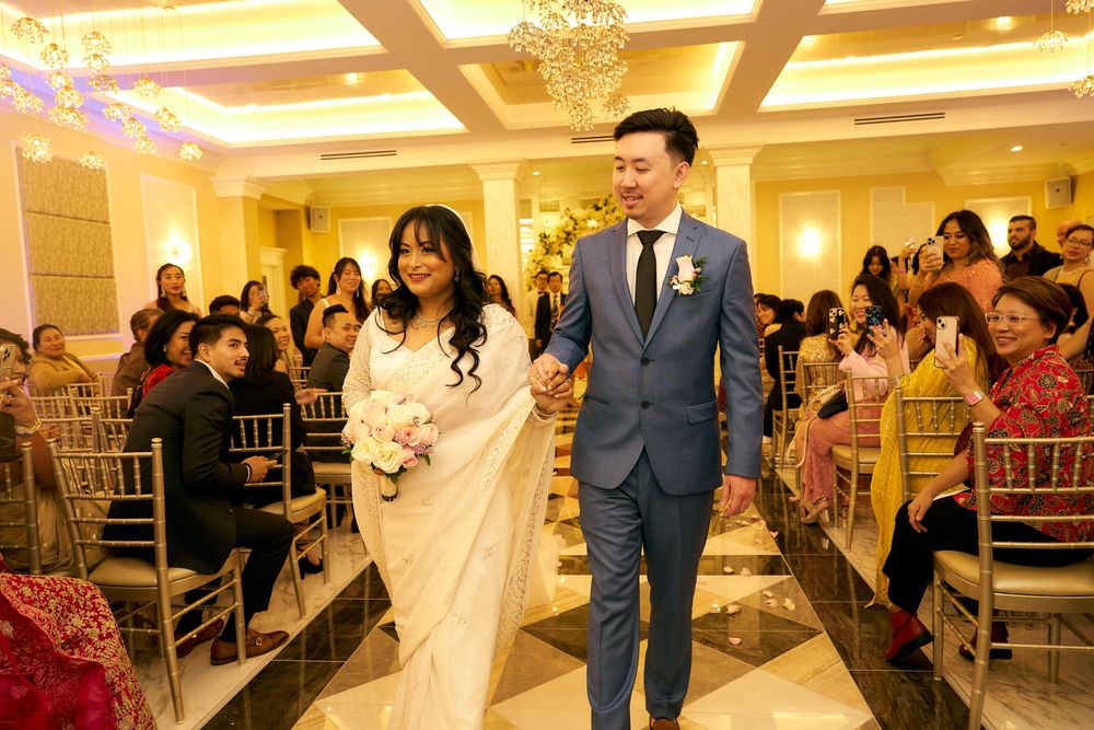 A wedding ceremony in an elegant ballroom with crystal chandeliers and guests seated in gold chiavari chairs.