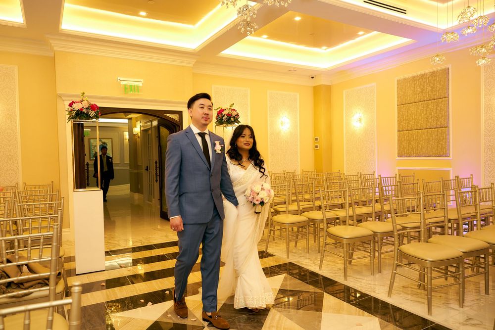 A couple standing in an elegant ceremony space with gold chairs and warm lighting.