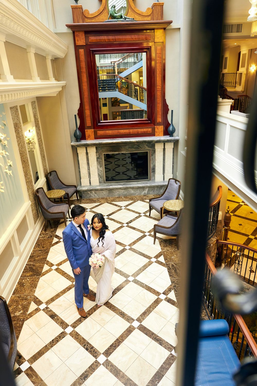 An artistic overhead view through railings of a couple on geometric marble flooring near antique furniture. at Jericho Terrace
