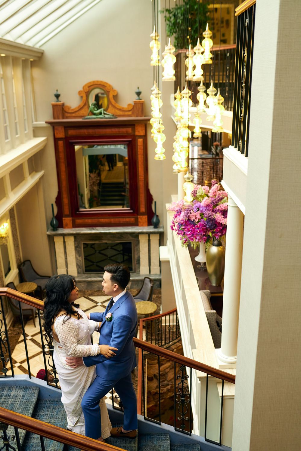 A couple taking romantic photos in an elegant hallway with white columns and hanging chandeliers. at Jericho Terrace
