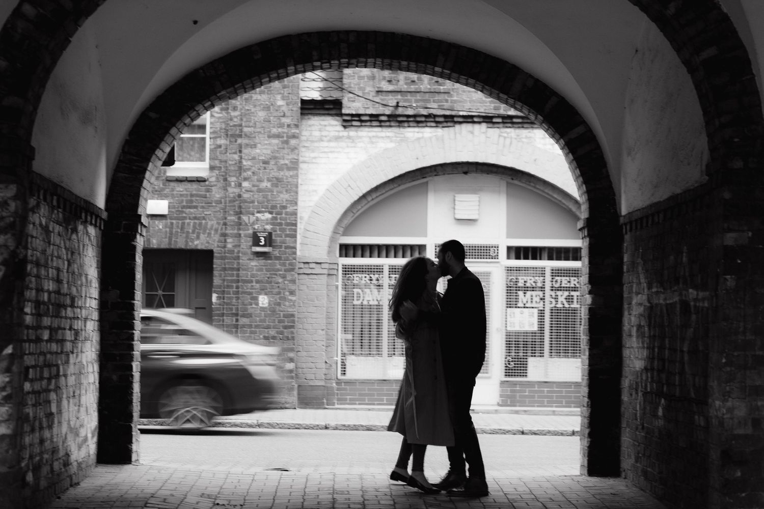 A romantic couple sharing an intimate moment in a dimly lit hallway with arched ceilings and ambient lighting.