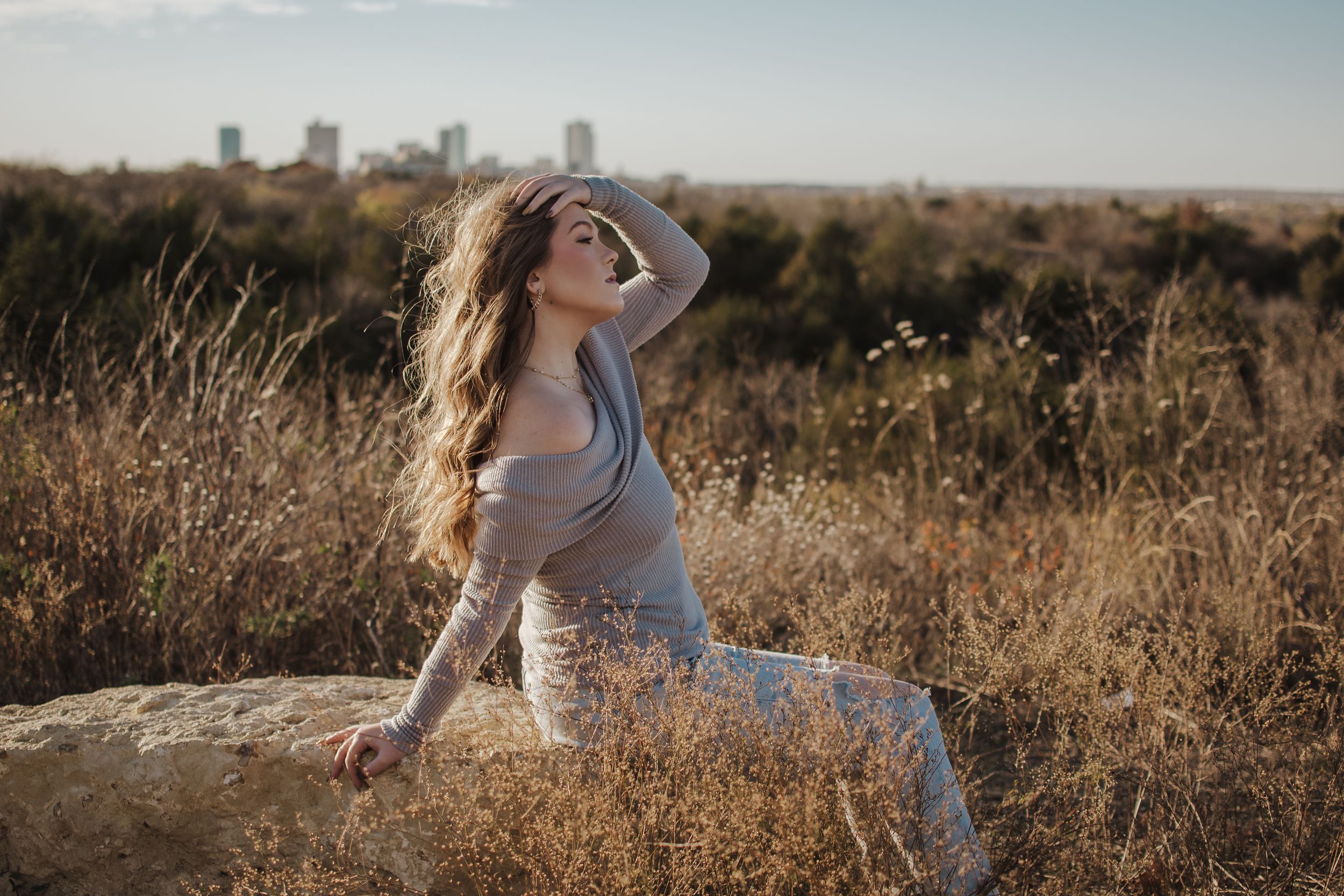 A dreamy sunset portrait in a golden field with a city skyline visible in the distance. Tandy Hills Senior Session