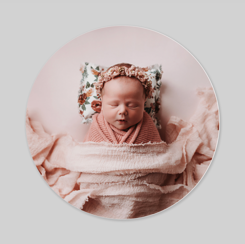 Newborn infant sleeping peacefully in soft, textured pink fabric with a delicate floral headpiece.