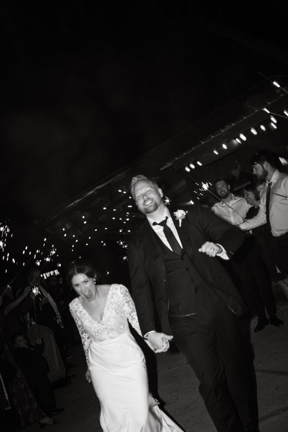 A black and white candid moment shows a wedding couple dancing and laughing during their nighttime celebration.