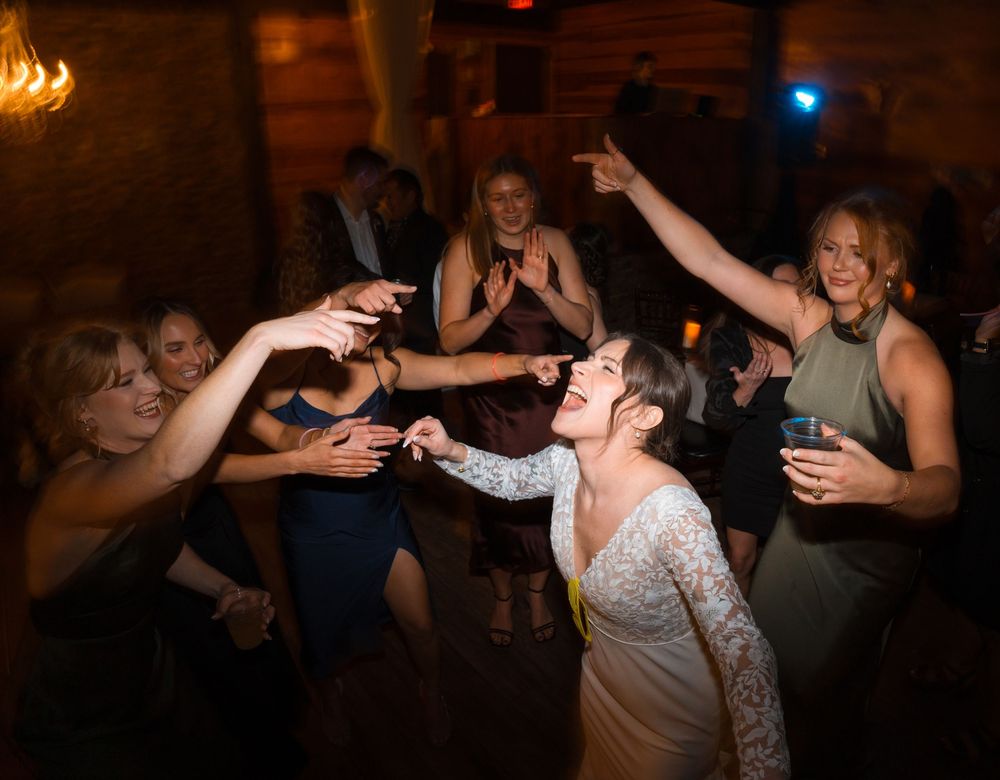 Partygoers dancing and raising drinks in celebration at a dimly lit venue with warm lighting.