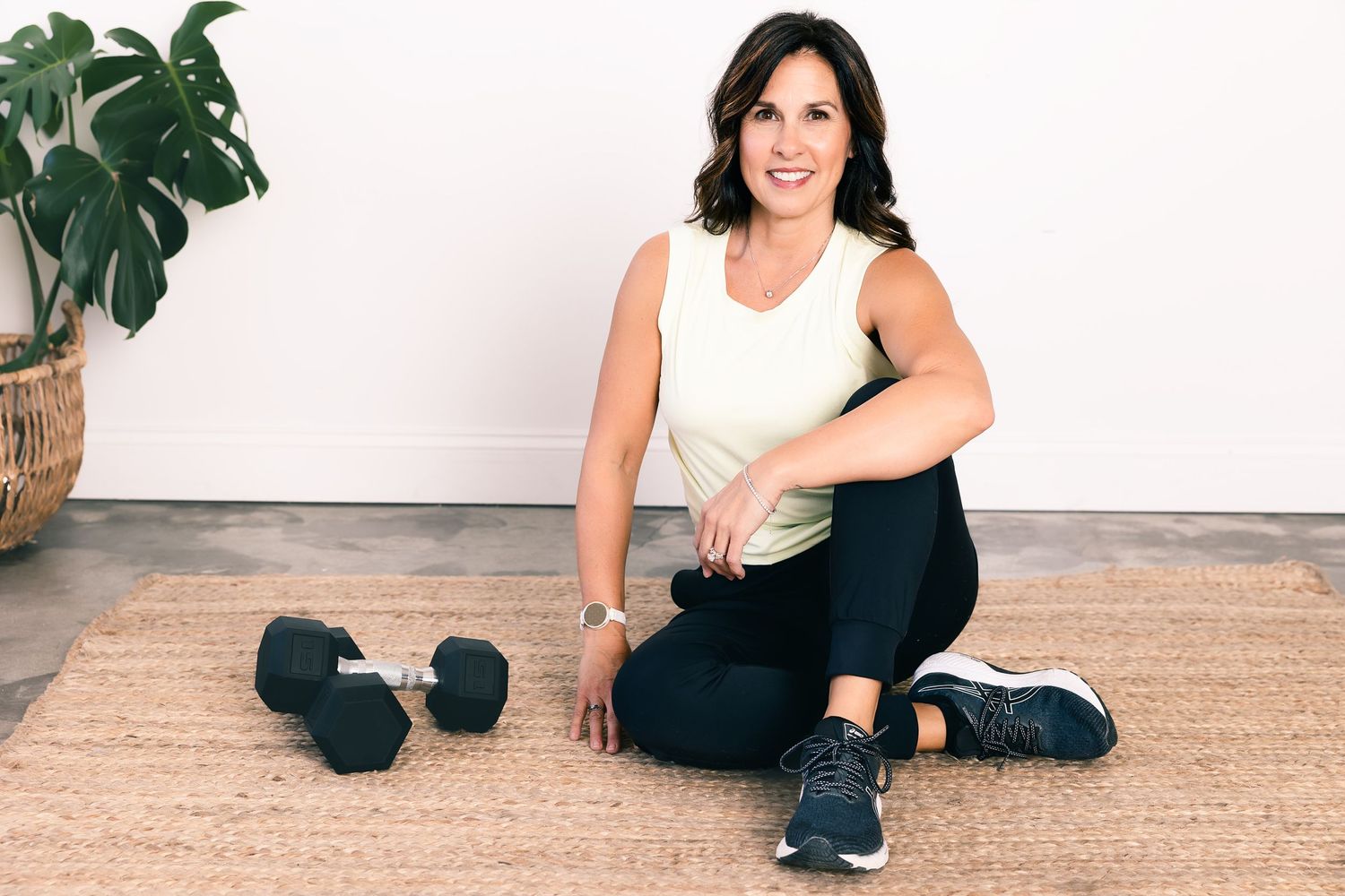 Person demonstrating stretches and workout movements on a mat in a minimalist home setting with monstera plant decor.