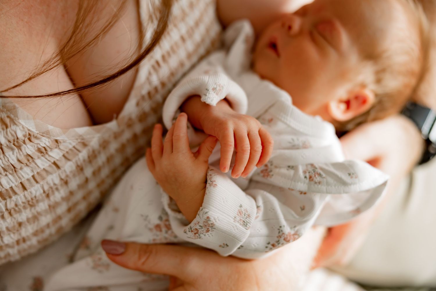 Newborn baby sleeps peacefully in white clothing while being gently held against a cozy knit sweater.