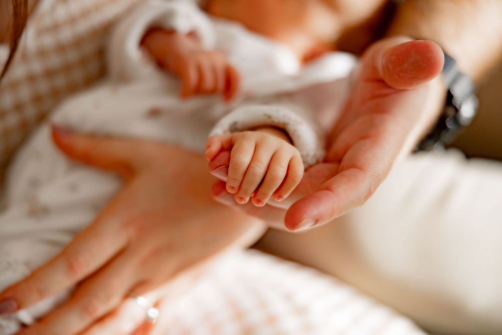 Gentle baby foot massage at home with moisturizing cream on soft beige background.