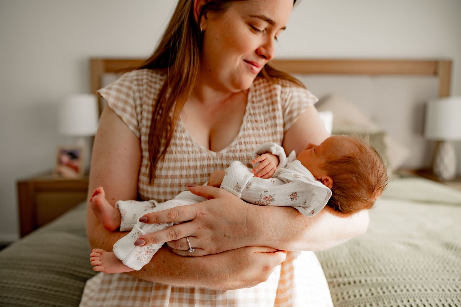 A tender moment between a mother and newborn baby in a cozy bedroom with natural lighting.
