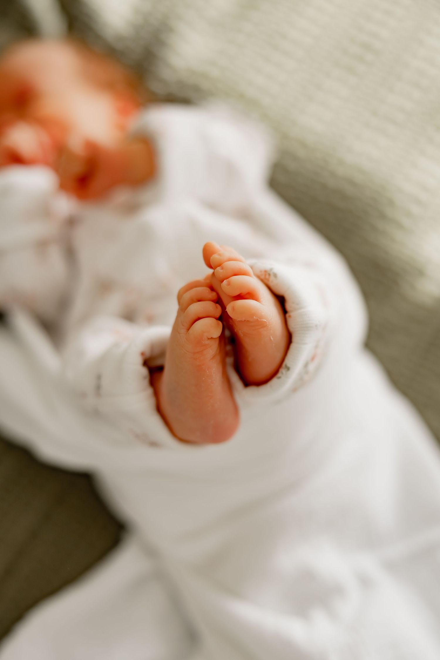 Close-up view of tiny baby feet in white clothing against a neutral background.