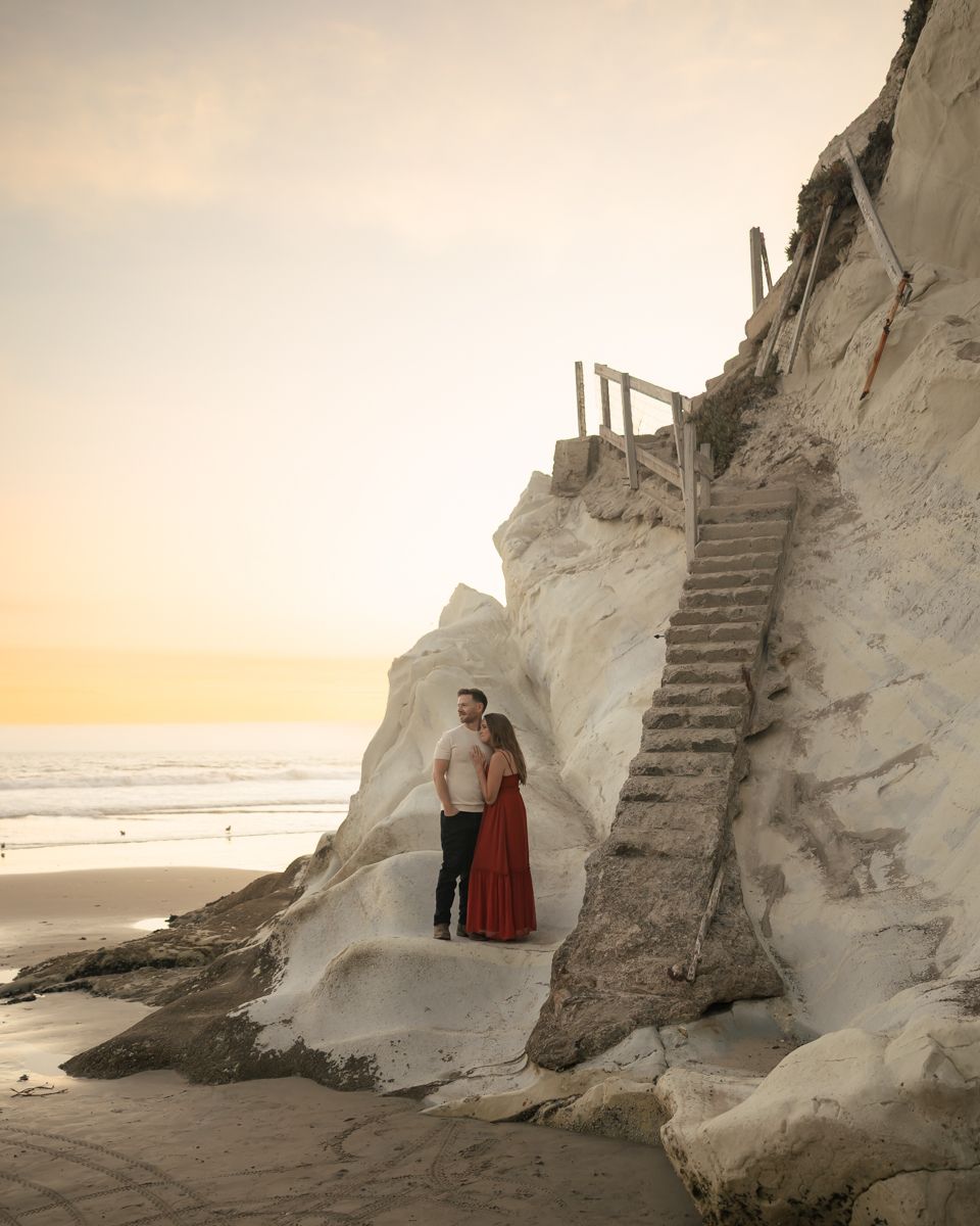 Sunset beach portrait with couple framed by dramatic white cliffs and coastal stairs.