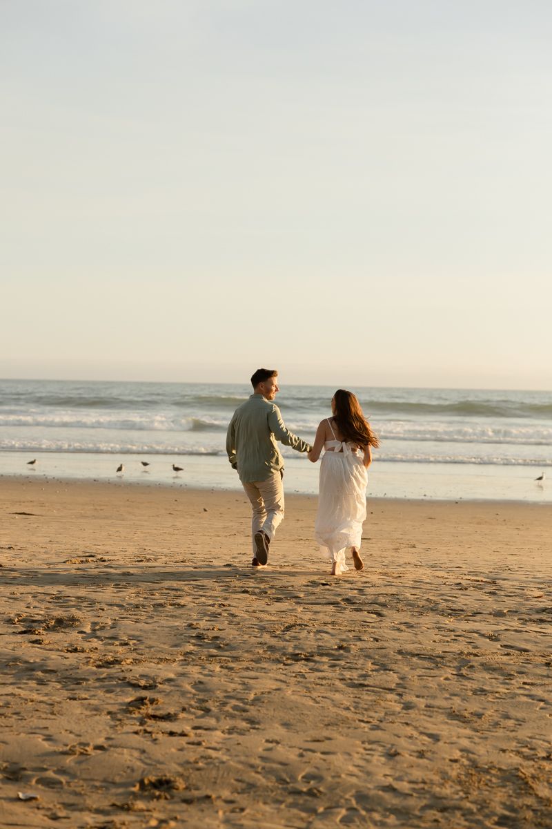 A couple walks hand in hand along a peaceful beach during golden hour.