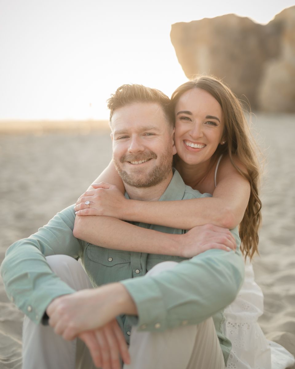 A joyful couple embracing and laughing together during a beach photoshoot at sunset.