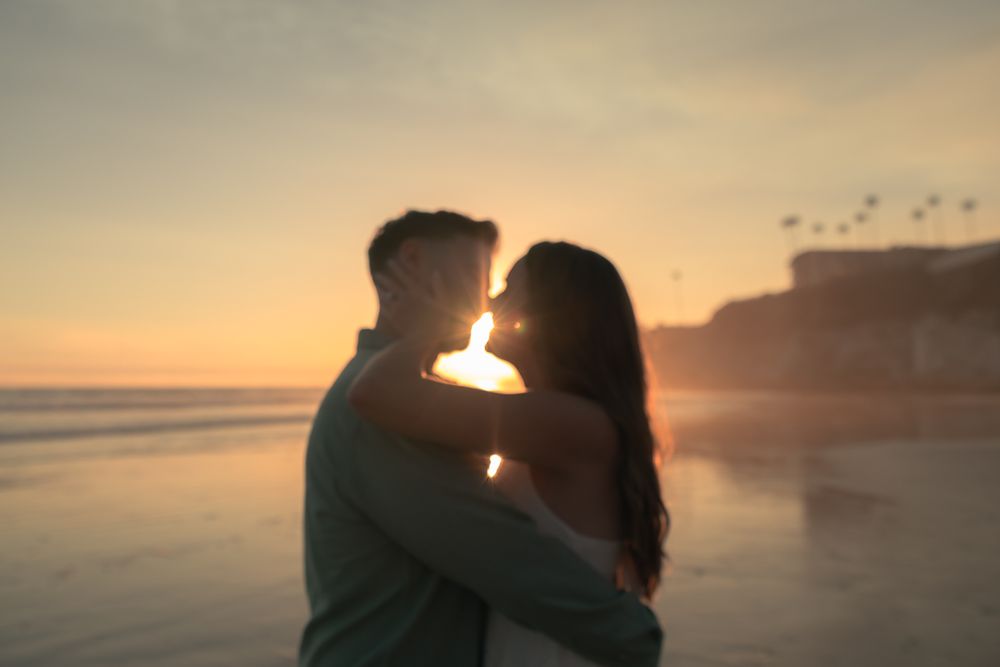 A romantic silhouette of two people embracing on the beach during golden hour.