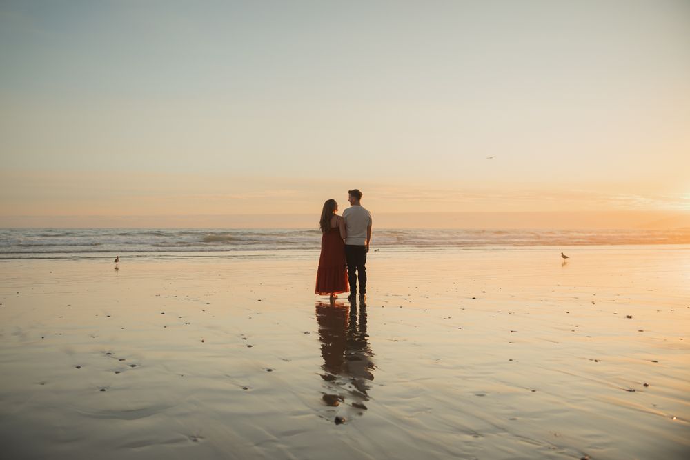 A couple watches the sunset together while standing in reflective waters on the beach.