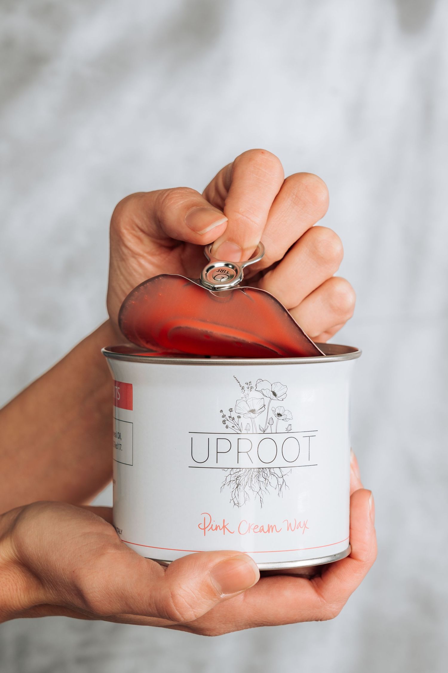 Hands holding an opened tin can of Uproot brand product with lid being pulled back to reveal red contents inside.