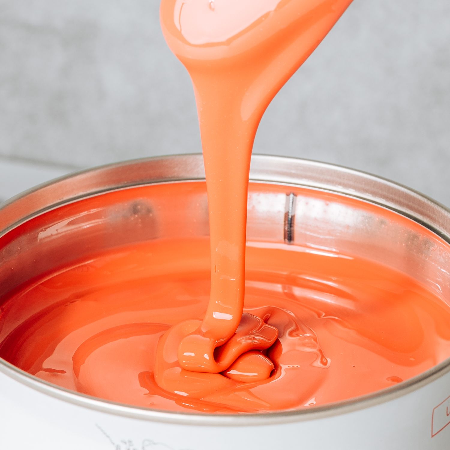 Bright coral pink liquid paint or coating being poured into a container showing smooth flowing consistency.