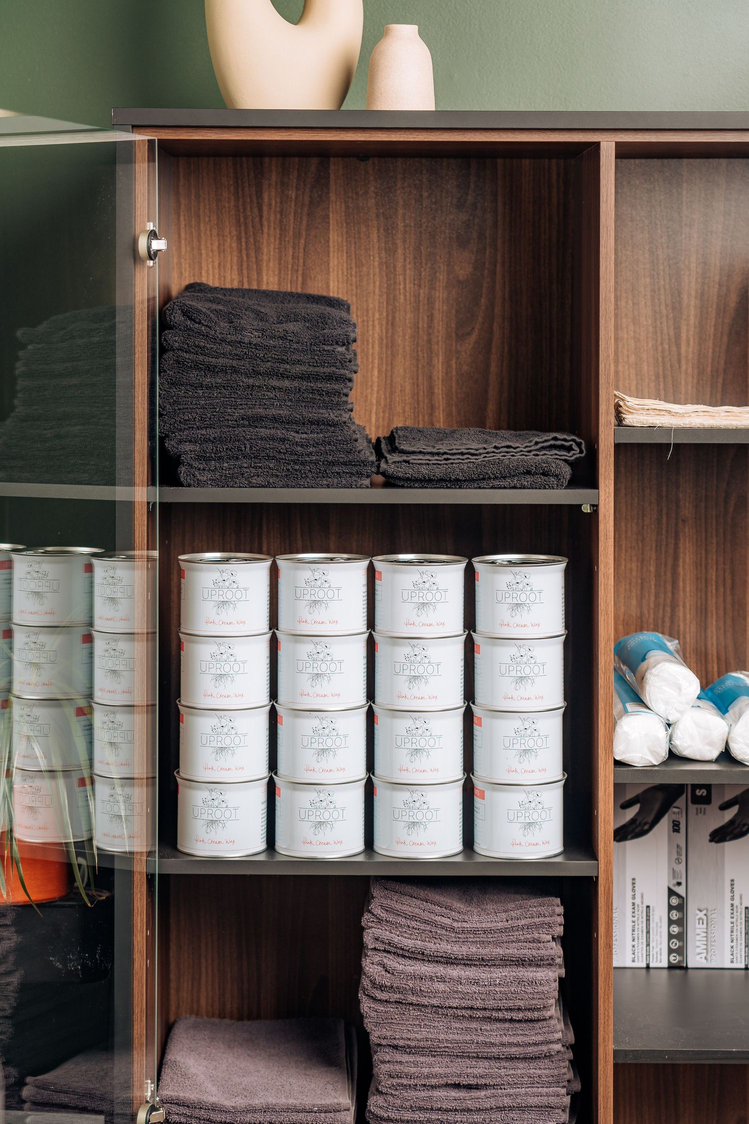 Wooden storage cabinet with neatly organized stacks of black and brown towels and white labeled containers on shelves.