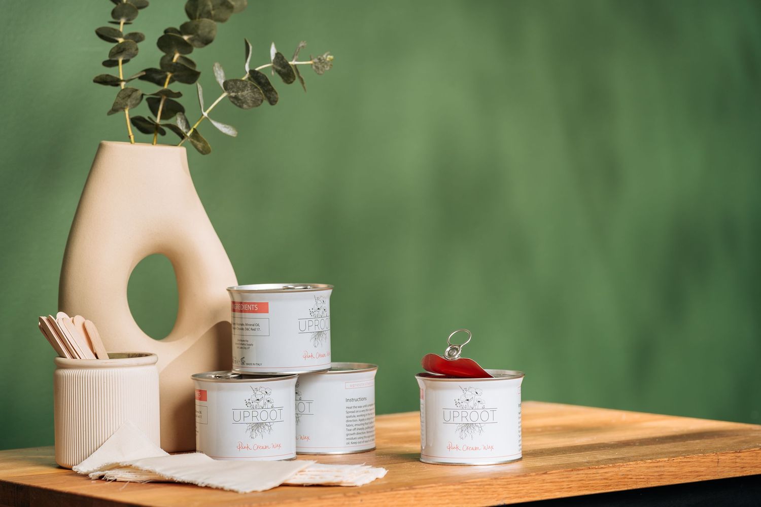 Modern minimalist home decor with ceramic vases, storage boxes and eucalyptus branches on wooden table against green background.