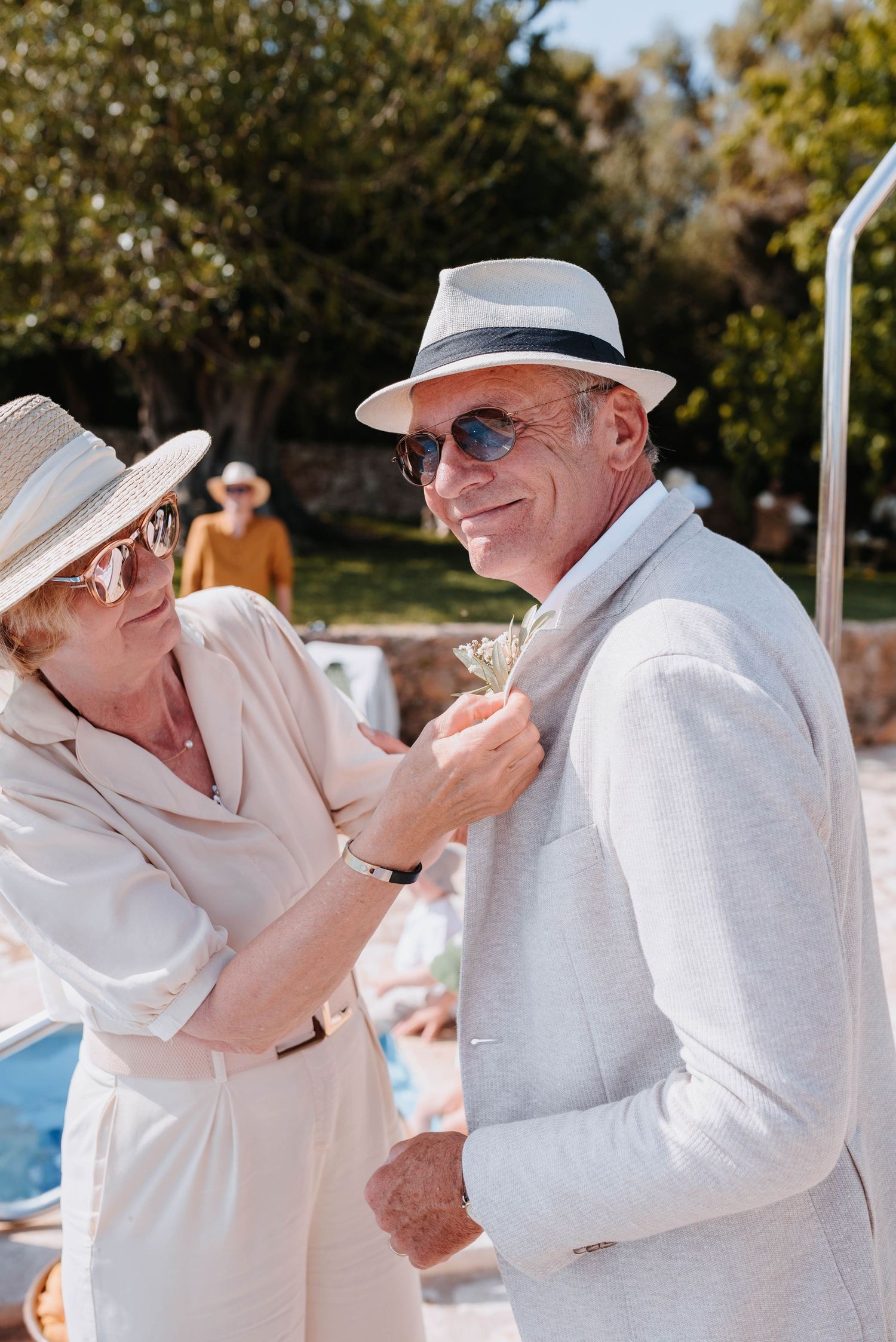 Ein älteres Paar in eleganter weißer Sommerkleidung genießt gemeinsam einen fröhlichen Moment bei einer Hochzeit im Freien.