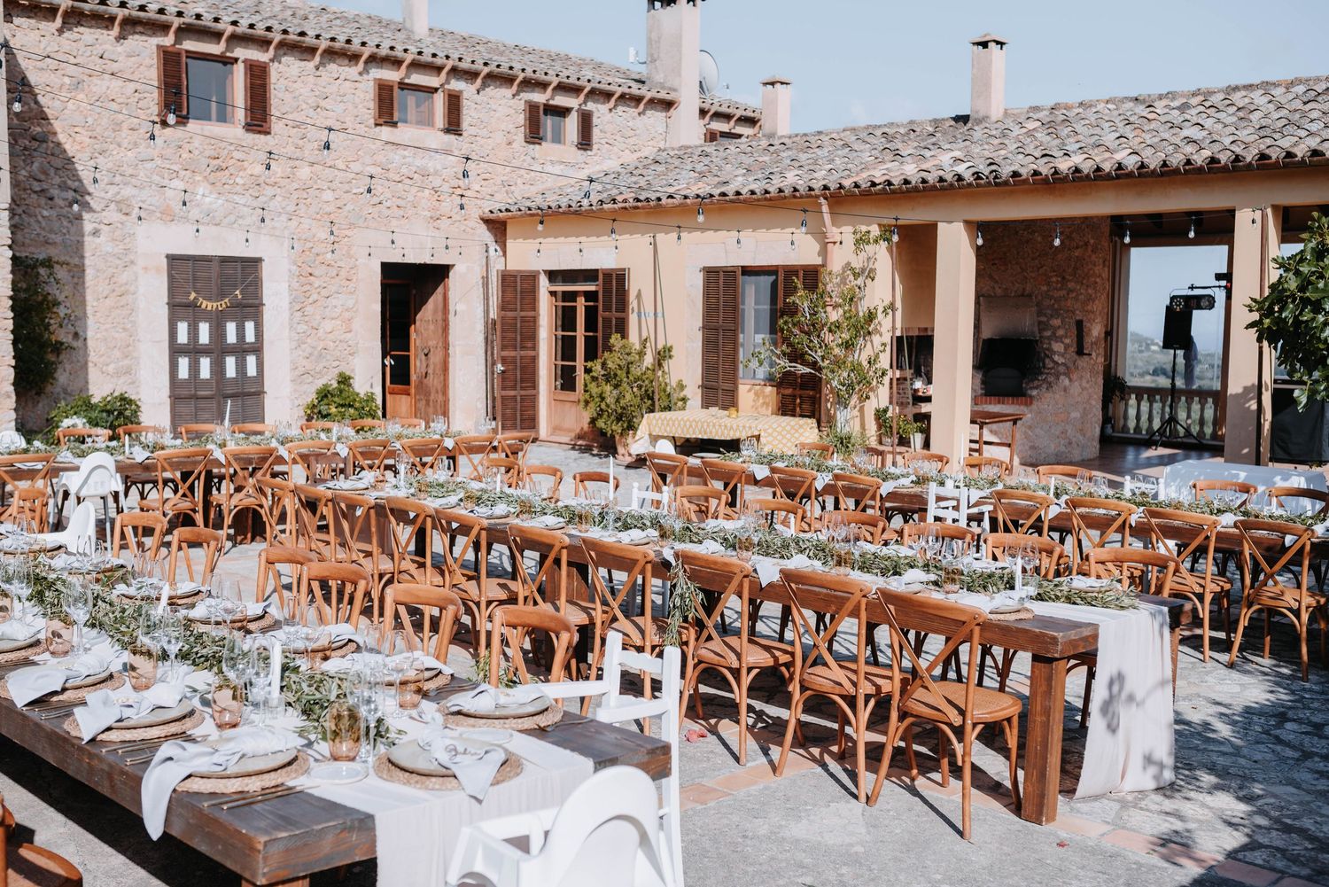 Reihen eleganter Tische für die Hochzeitsfeier im Freien, die in Reihen in einem rustikalen Innenhof im spanischen Stil aufgestellt sind.
